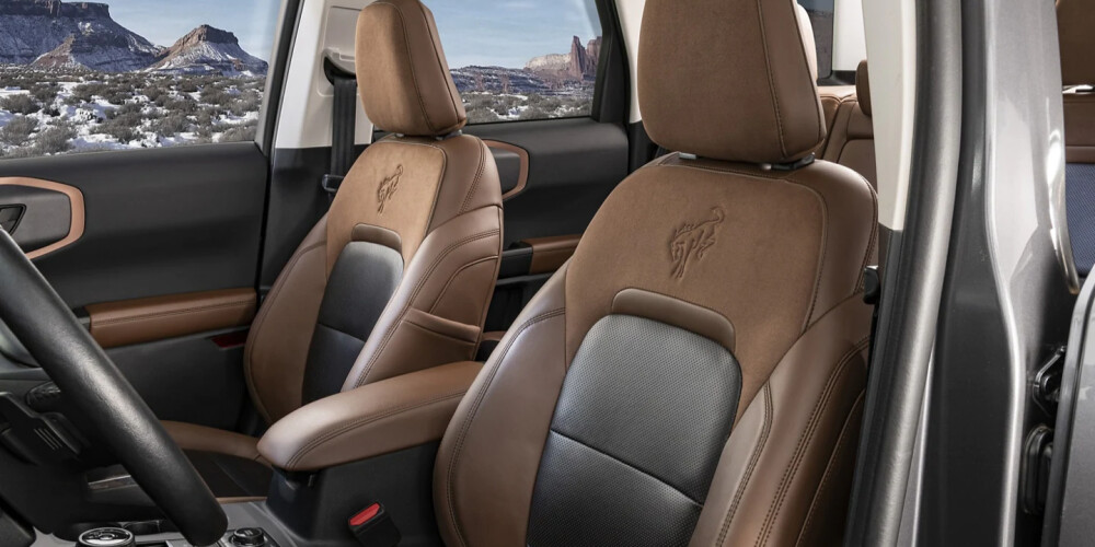 Front seats of an SUV with brown leather upholstery featuring an embossed logo. Snowy desert landscape visible through windows, conveying adventure.