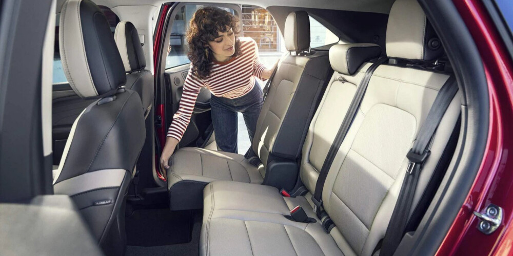 A woman in a striped shirt adjusts the rear seats of a red car. The car interior is spacious with light gray upholstery, conveying a modern and practical feel.