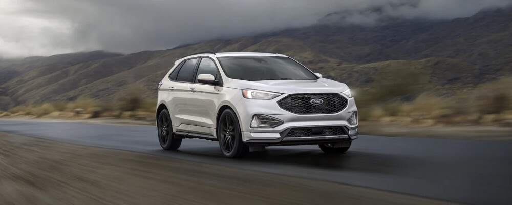 Silver SUV driving on a wet road with mountainous, overcast background. The scene conveys a sense of adventure and resilience in nature.